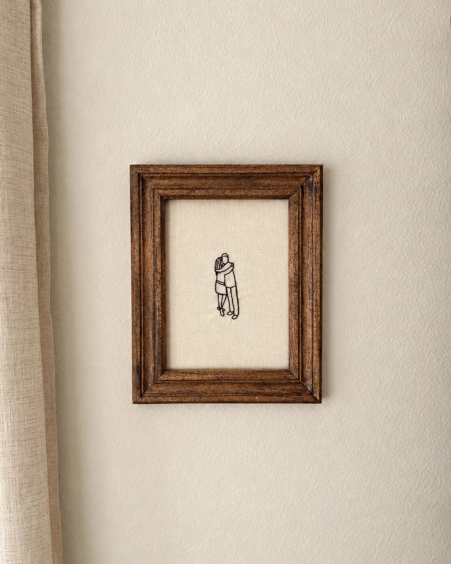 Hand-embroidered line drawing of a couple hugging, framed in dark wood by Bailey Langston